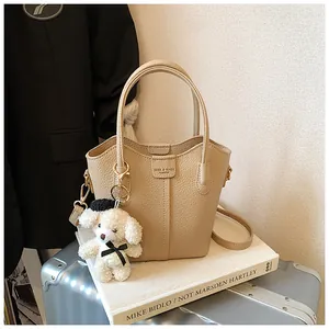 Stylish beige textured bucket bag with cute teddy charm on an art book setup.