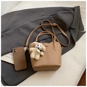 Close-up of chic khaki bucket bag with teddy bear charm and textured leather finish