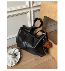 Vintage black hobo shoulder bag with plush bear charm displayed in a cozy room setting