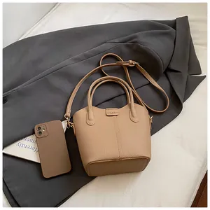 Beige pebble leather bucket handbag with top handles and adjustable shoulder strap