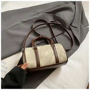 Detailed view of khaki cylindrical Boston bag with brown leather handles and trim