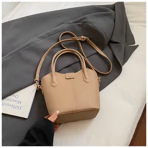 Stylish beige bucket bag with top handle and shoulder strap shown in a lifestyle setting