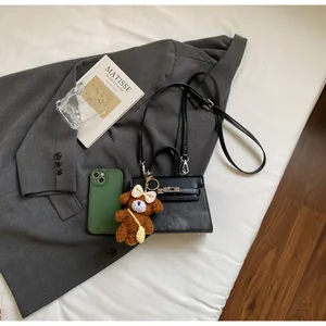 Elegante schwarze Lederhandtasche mit Silberverschluss und Teddybär-Anhänger auf Grau