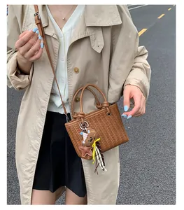 Detail einer braunen geflochtenen Beuteltasche mit Bärenanhänger an der Schulter.