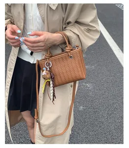 Nahaufnahme einer braunen gewebten Handtasche mit niedlichem Bärenanhänger für Damen.