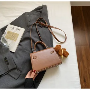 Detail einer braunen Kunstledertasche mit Plüschbären-Anhänger auf grauem Blazer-Hintergrund