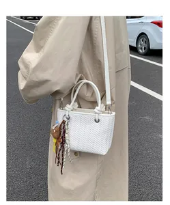 Detailansicht einer weißen geflochtenen Eimertasche mit bunten Anhängern am Trenchcoat