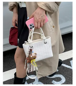 Detailaufnahme einer weißen gewebten Handtasche mit einem süßen braunen Bärenanhänger