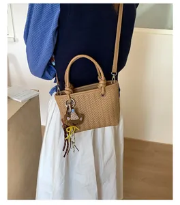 Detailansicht einer khakifarbenen gewebten Handtasche mit süßem Bärenanhänger für den Alltag.