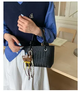 Detailaufnahme einer schwarzen geflochtenen Handtasche mit einem niedlichen Bärenanhänger