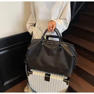 Grand sac de voyage noir en nylon avec bandoulière placé sur une valise blanche