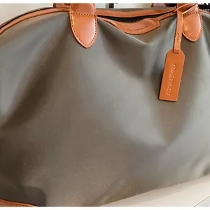 Détail d'un sac de voyage en nylon vert olive avec finitions en cuir marron et étiquette.