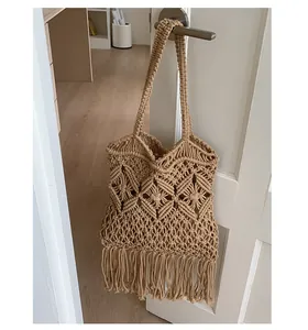 Handmade macrame tote bag with long fringe tassels hanging on a minimalist door handle