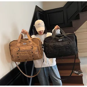 Comparison of black and brown large travel bags held by a model on a modern staircase