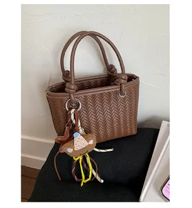 Detailansicht einer braunen Tasche mit Webstruktur und süßem Bären-Schlüsselanhänger