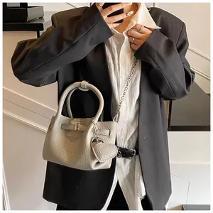 Close-up of minimalist pebbled bucket bag being worn with a blazer and heart charm