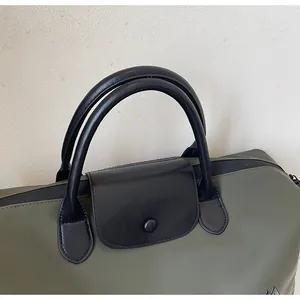 Detail view of green travel bag showing black leather handles and snap closure flap.