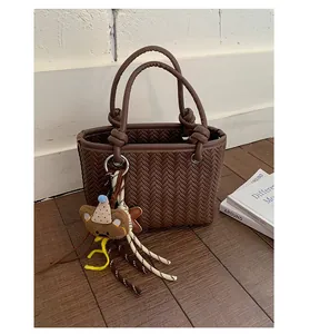 Nahaufnahme einer braunen geflochtenen Eimertasche mit einem süßen Bärenanhänger