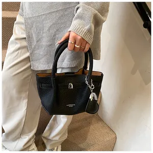 Close-up of elegant black lychee textured leather bucket bag carried by hand in a stylish setting