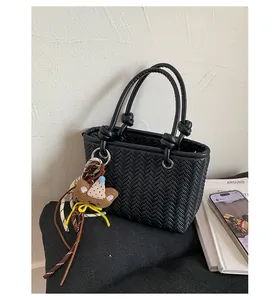 Detailansicht der schwarzen gewebten Handtasche mit süßem Bärenanhänger im Lifestyle