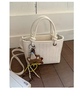 Detailansicht einer cremeweißen gewebten Beuteltasche mit süßem Braunbären-Anhänger-Accessoire
