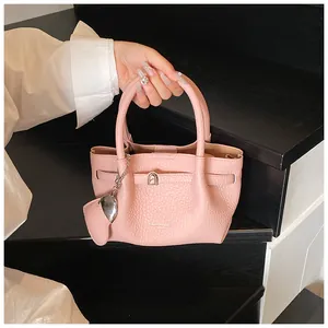 Detailed view of elegant pink lychee grain handbag featuring a metallic buckle and heart charm