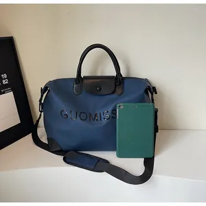 Detail view of large blue travel bag with GUOMISS letter print and a tablet for size reference