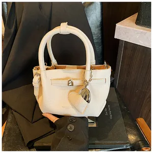 Close-up view of a minimalist cream bucket bag with litchi texture and heart charm