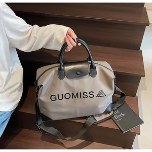 Spacious beige travel handbag featuring black GUOMISS text print on stylish wooden stairs.