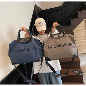 Model holding two large travel bags in navy blue and khaki color on a staircase