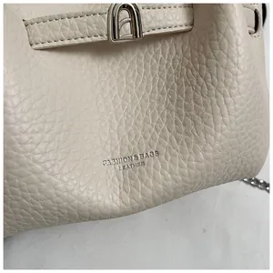 Close-up detail showing the lychee pattern leather texture on a beige bucket bag