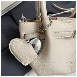 Close-up of beige lychee pattern leather bucket bag with heart-shaped charm detail