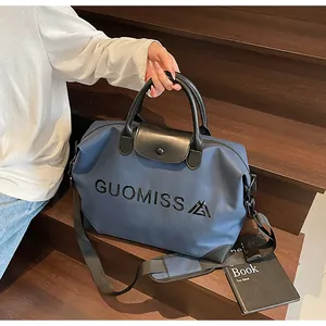 Close-up detail of a large blue travel bag featuring embossed GUOMISS logo and leather accents