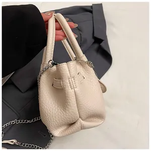 Close-up detail of a minimalist cream lychee grain textured handbag with silver chain strap