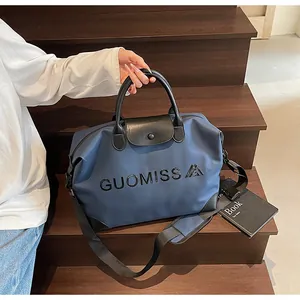 Detail of large blue travel bag with GUOMISS embossing and black leather handles