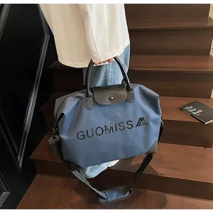 Detailed view of large blue travel bag with GUOMISS lettering and black leather trim.