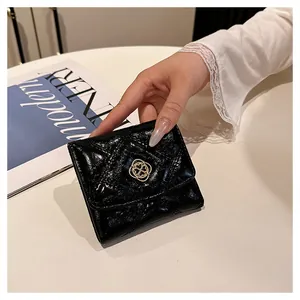 Detail view of a glossy black quilted short wallet with elegant gold floral emblem.