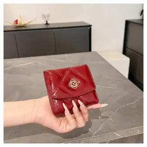Detail showing red glossy quilted mini wallet with gold clover clasp in hand