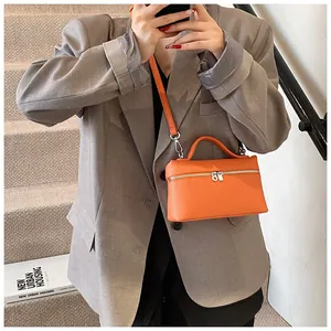 Foto de estilo de vida de un bolso bandolera de PU naranja con un blazer gris chic.