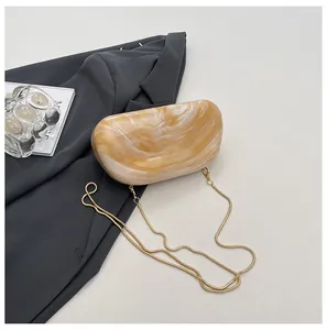Detailed view of an amber marble acrylic clutch bag with a gold metal chain strap