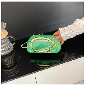 Close-up of a green marble-patterned mini clutch bag featuring a bold golden metal handle
