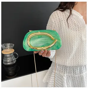 Detail of green marbled acrylic clutch bag with iconic gold C-shaped metal handle and chain