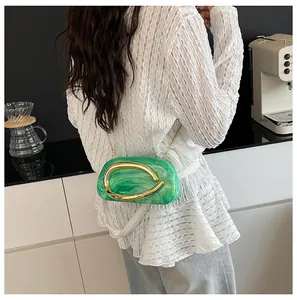 Detail of a green marble acrylic evening bag with gold handle worn by a model in a kitchen.