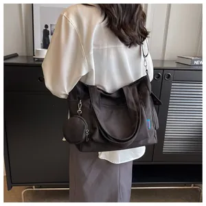 Detailed view of a black canvas tote bag with a small coin purse charm on a model's shoulder.