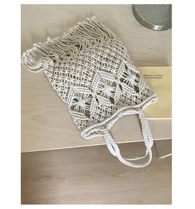 Close-up detail of cream macrame tote bag with long fringe and bohemian knit patterns.