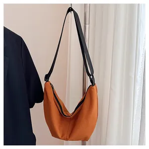 Primer plano de un bolso hobo naranja grande con correa negra colgado de un perchero.