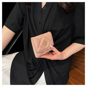 Close-up detail of a pink quilted short wallet with gold-tone buckle held by a model