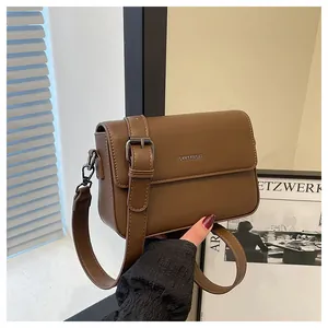 Vintage brown leather crossbody square bag held against a minimalist background