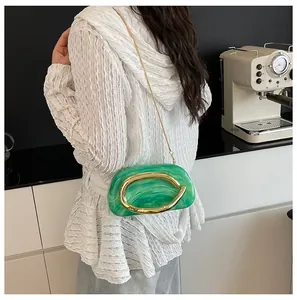 Detail view of a green marble-patterned round evening clutch bag with gold handle worn by a model