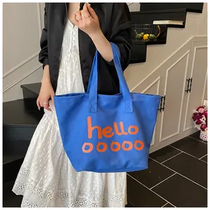Grande bolso tote de lona azul con estampado naranja hello llevado por una modelo